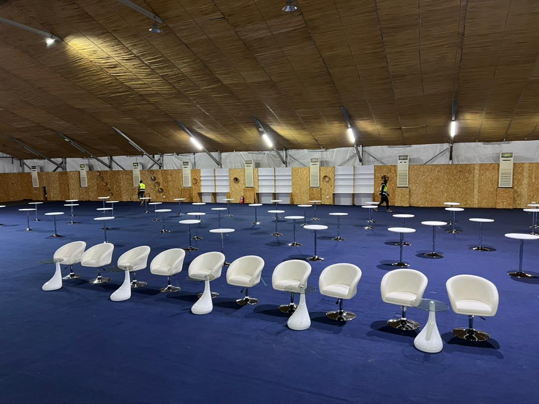 Rows of white lounge chairs and cocktail tables inside a giant event tent